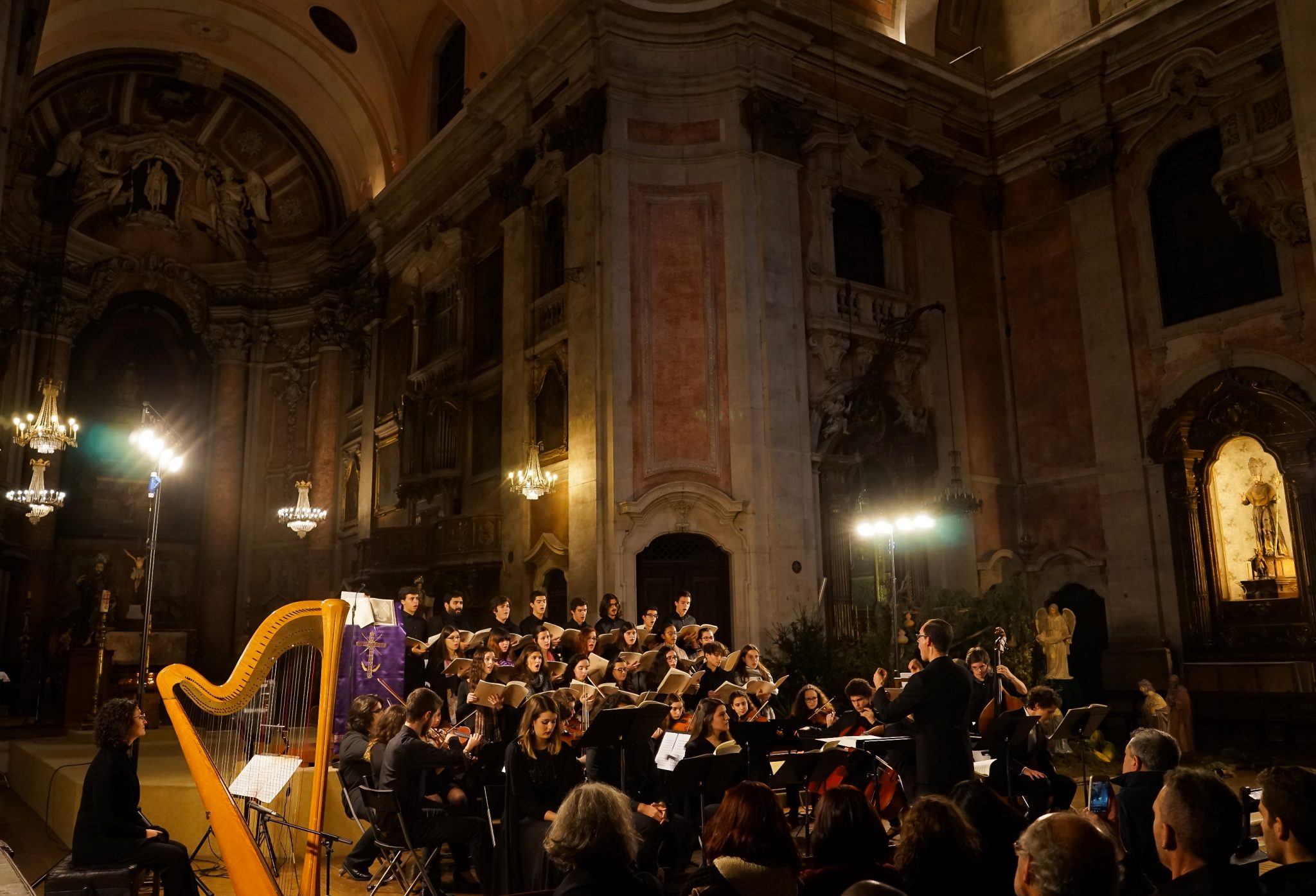 No cenário de uma igreja, um concerto que inclui uma harpa, instrumentos de corda e um coro
