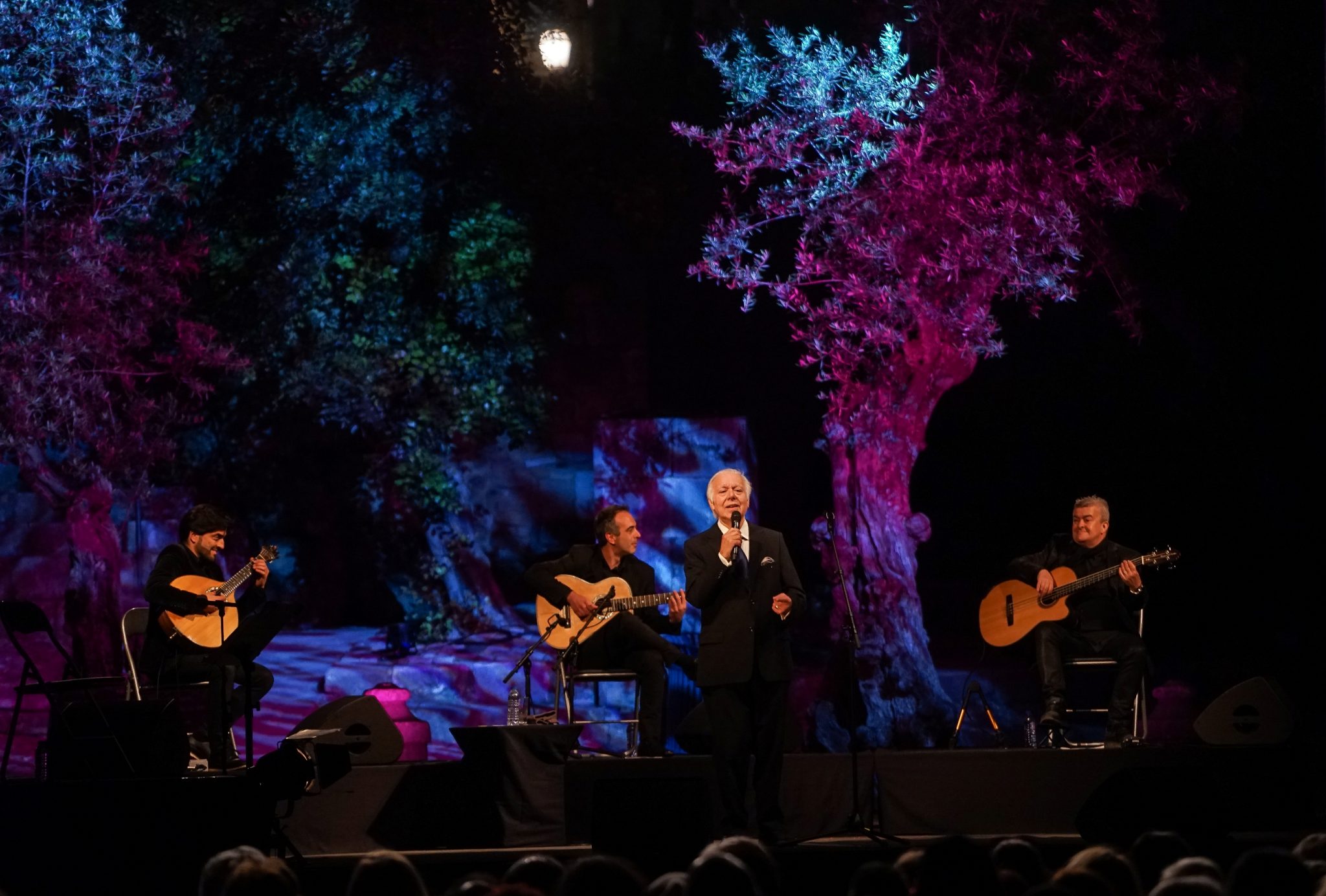 Vista do palco do concerto de Carlos do Carmo, com o fadista ao centro de pé rodeado pelos músicos à esquerda e à direita.