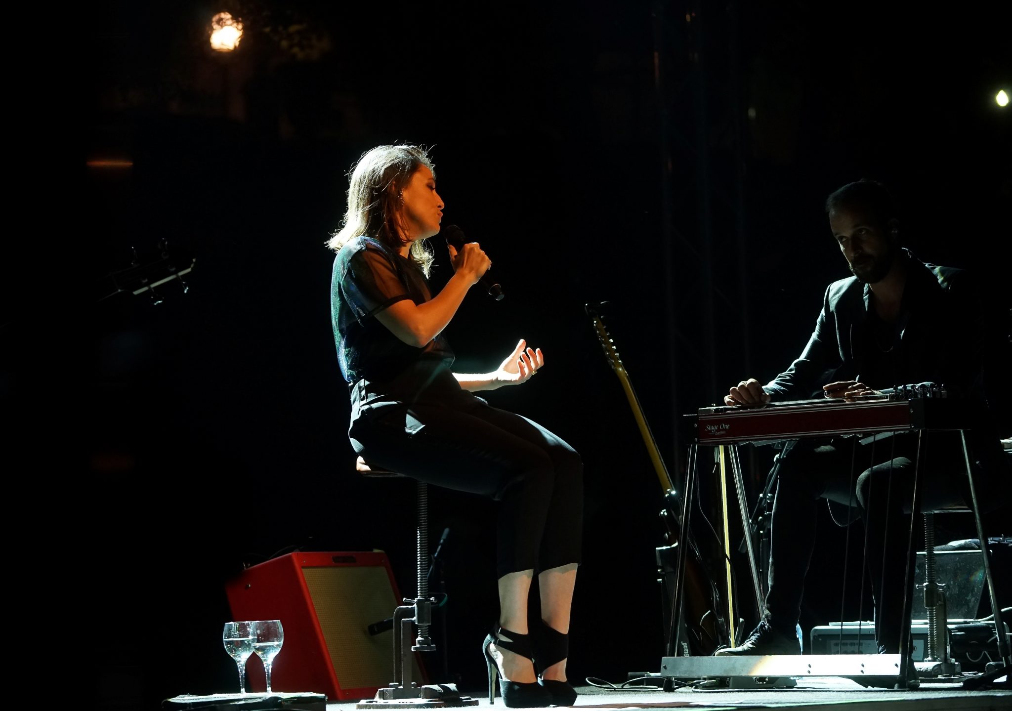 A fadista Carminho sentada, à esquerda, olhando para o músico Tomara, à direita.
