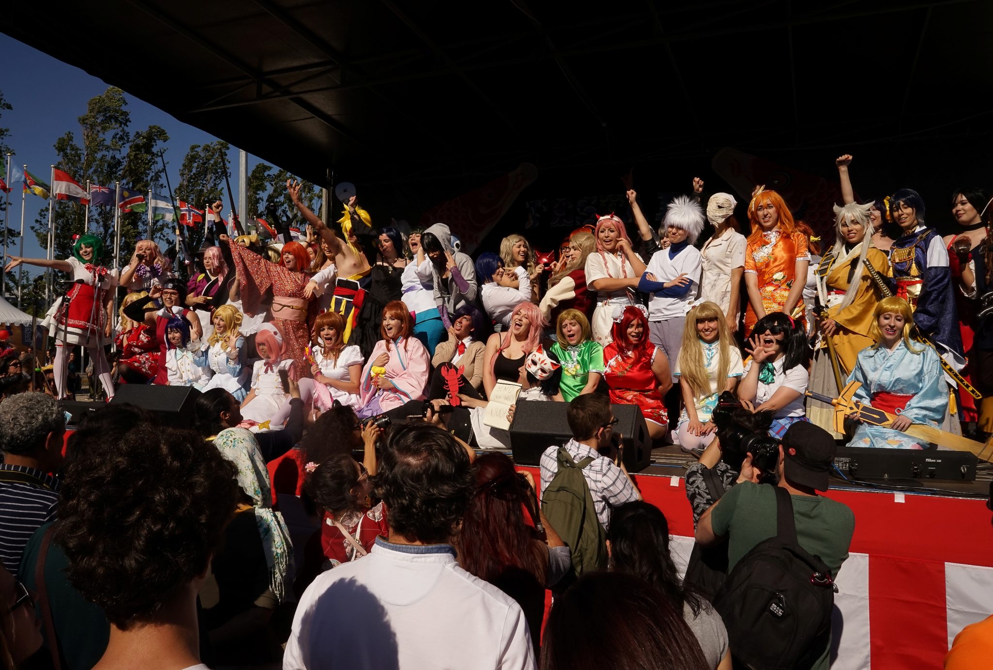 Em cima de um palco, vários praticantes de cosplay posam para os fotógrafos a sorrir.