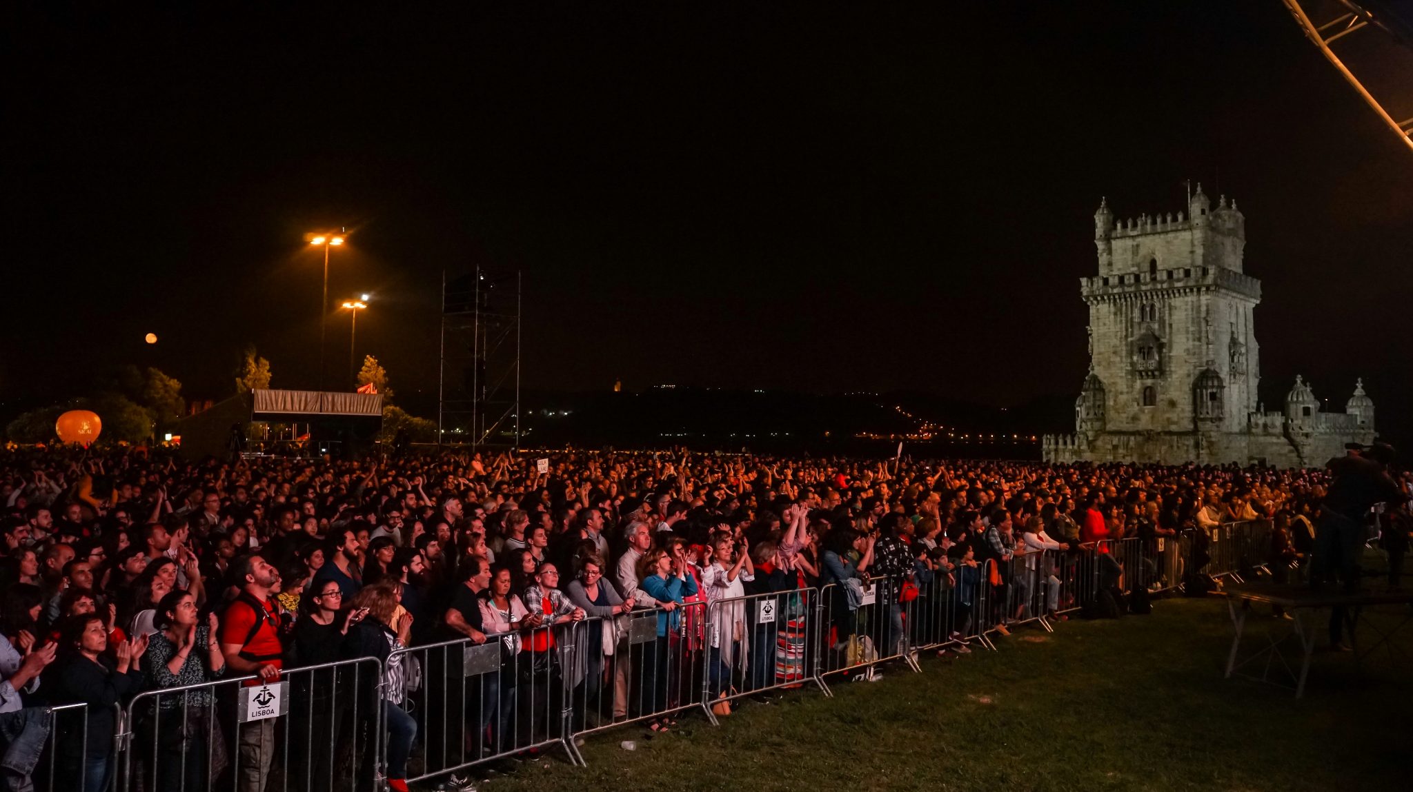 Visão geral dos milhares de espetadores do concerto Refavela 40 a partir do palco, com a Torre de Belém ao fundo